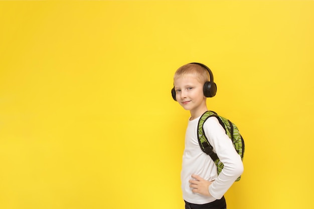 Menino loiro com uma mochila nas costas e fones de ouvido em um fundo amarelo com espaço de cópia de volta à escola