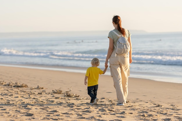 Menino loiro e sua mãe caminhando na praia