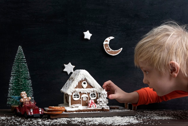 Menino loiro faz composição de Natal da casa de pão de mel, carro de brinquedo e árvore de Natal.