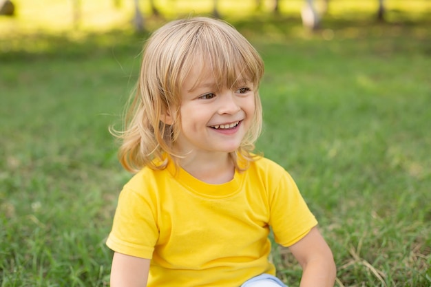 menino loiro feliz sentado no gramado em um sorriso dentuço de camiseta amarela