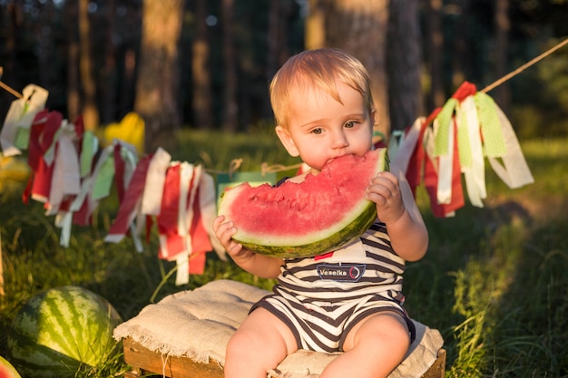 Menino loiro fica cercado por melancias em um dia de verão