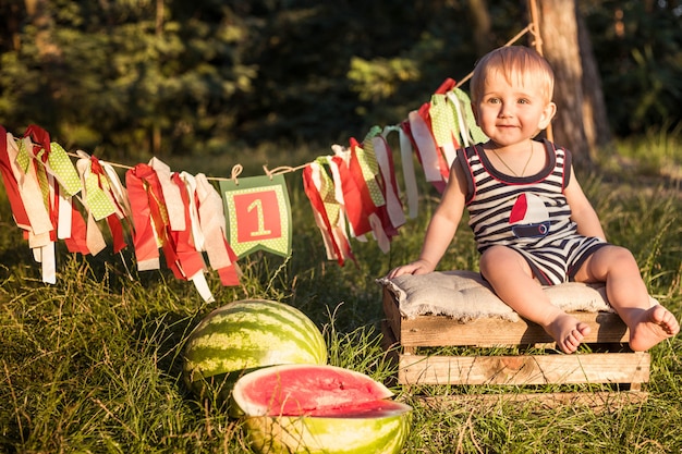 Menino loiro fica cercado por melancias em um dia de verão