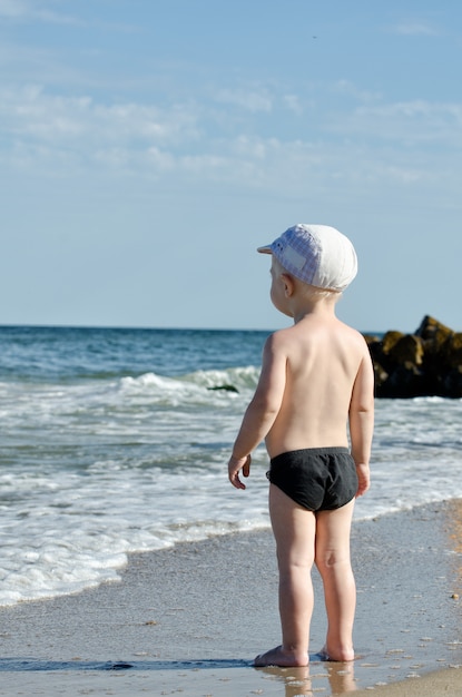 Menino loiro na praia olhando as ondas