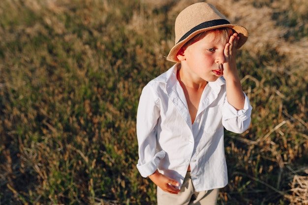 Menino loiro no chapéu de palha, jogando no campo no feno segado. verão, tempo ensolarado, agricultura. infância feliz.