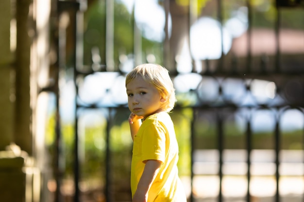 Menino loiro no parque em pé perto dos portões