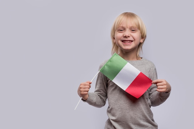 Menino loiro segurando a bandeira da Itália e ri Estudo da língua italiana