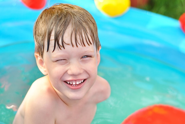 Menino loiro sorridente na água azul no verão na piscina