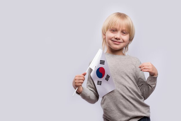 Menino loiro sorrindo e segurando bandeira da coreia do sul