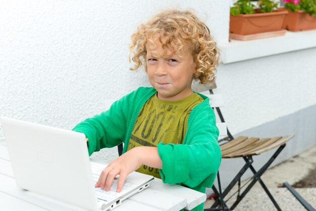 Menino loiro usando um laptop, ao ar livre