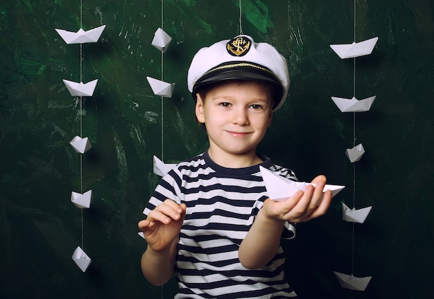 Menino marinheiro de chapéu com muitos barcos de papel, sonhos de infância e passatempo