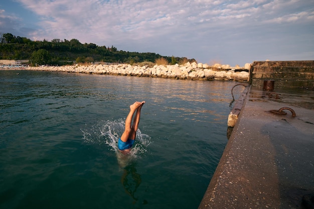 Menino mergulha no mar de um cais dia de verão quente