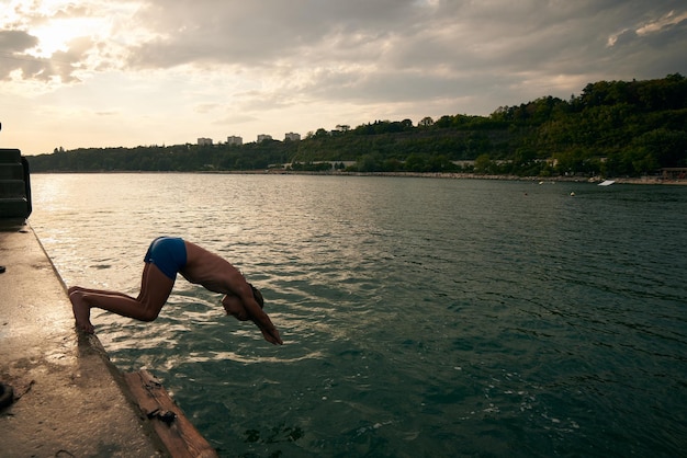 Menino mergulha no mar de um cais Dia de verão quente