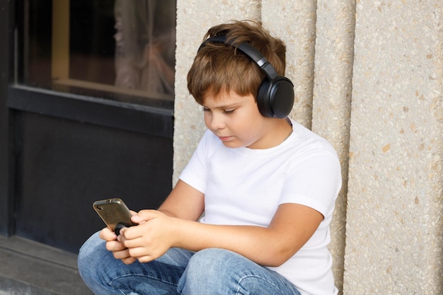 Menino moderno em fones de ouvido com smartphone ouvindo música no parque