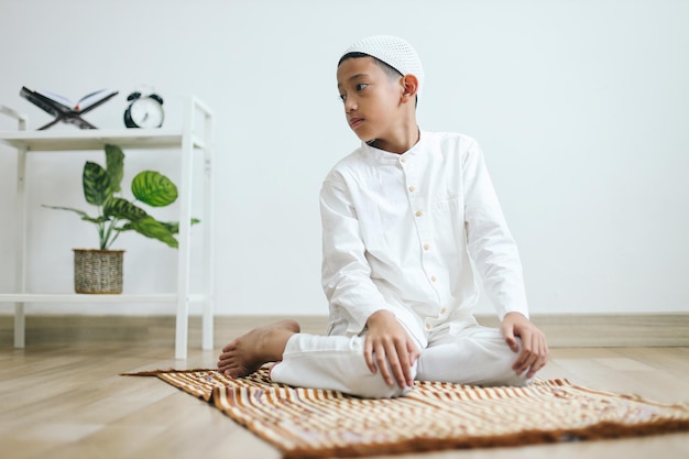 menino muçulmano vestindo capuz rezando salat em posição sentada recitando o salam voltado para a direita d