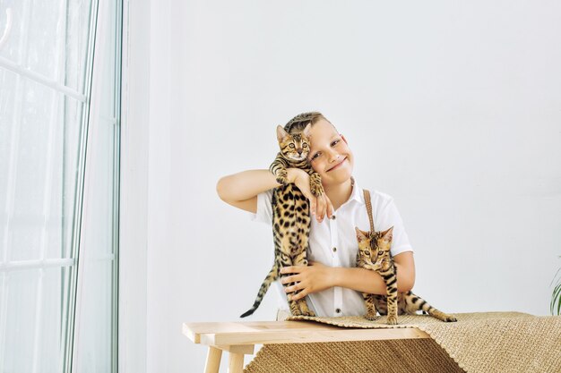 Menino na moda lindo e feliz com gatinhos fofos de Bengala juntos