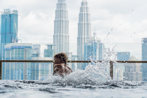 Menino na piscina ao ar livre com vista da cidade no céu azul