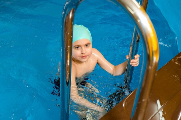 Menino nadando na piscina coberta e se divertindo durante a aula de natação