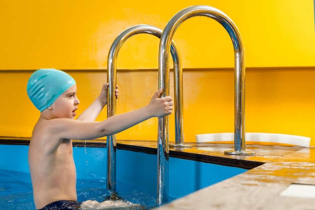 Menino nadando na piscina coberta e se divertindo durante a aula de natação