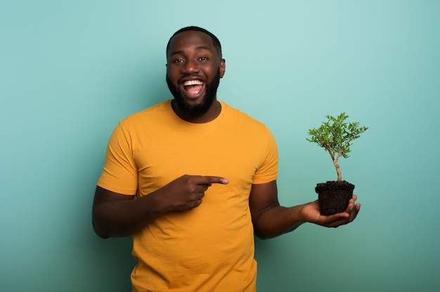 Menino negro feliz indica uma pequena árvore pronta para ser plantada