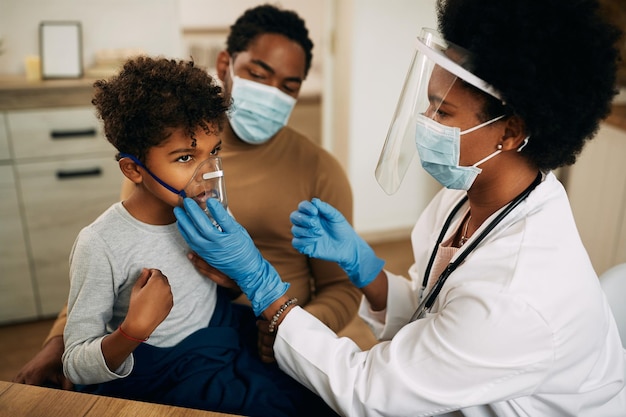Menino negro recebendo tratamento de asma enquanto o médico o visita em casa devido à pandemia covid19