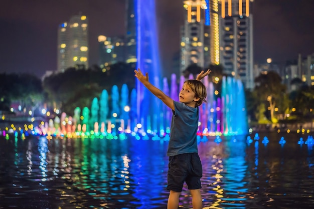 Menino no fundo da fonte colorida no lago à noite perto de Twin Towers com cidade no fundo Kuala Lumpur Malásia