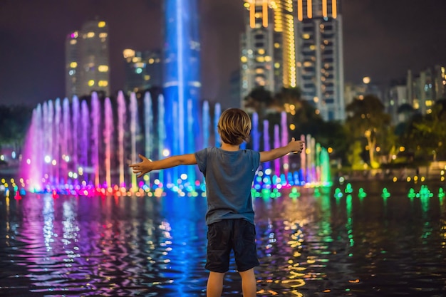 Menino no fundo da fonte colorida no lago à noite perto de Twin Towers com cidade no fundo Kuala Lumpur Malásia