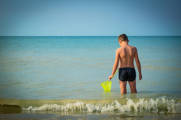 Menino no mar. a criança vai para o mar com uma rede para caçar borboletas. conceito de férias durante as férias de verão