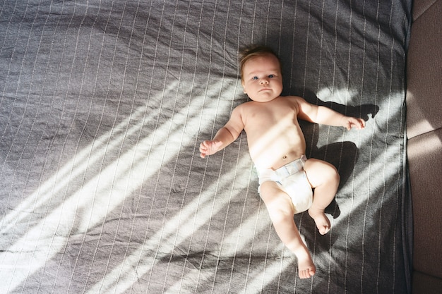 Foto menino nu recém-nascido estava deitado na cama sob os raios de sol saindo pela janela