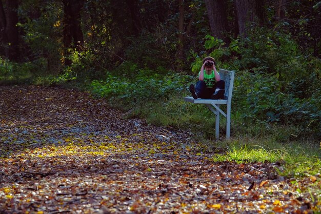 Foto menino olhando através de binóculos enquanto estava sentado em um banco no parque