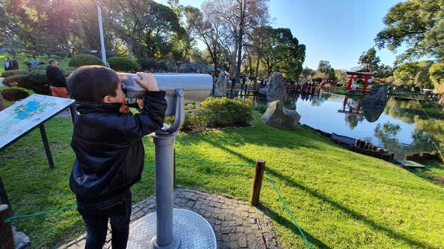 Foto menino olhando através de binóculos operados por moedas contra o lago no parque