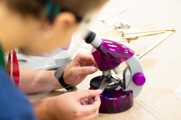 Menino olhando através de um microscópio roxo para uma pena de pássaro em um evento de ciências infantil