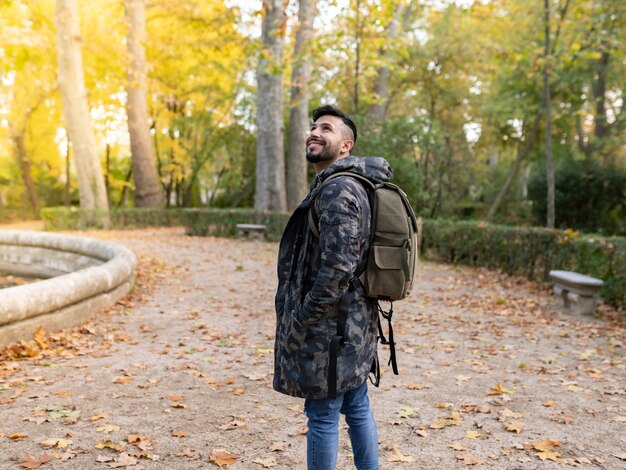 Menino olhando para o céu, em uma floresta, usa mochila e casaco com capuz, aventureiro