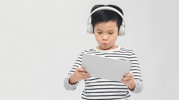 Menino ouvindo música ou assistindo filme com fones de ouvido e usando tablet digital tocando