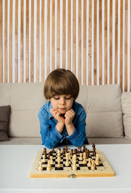 Foto menino pensativo se senta a uma mesa e joga xadrez em uma sala