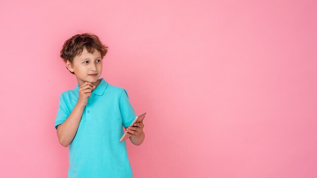 Foto menino pensativo tem smartphone nas mãos e parece longe no rosa.