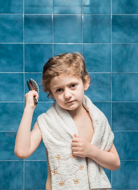 Foto menino penteando o cabelo enquanto está de pé contra a parede de azulejos