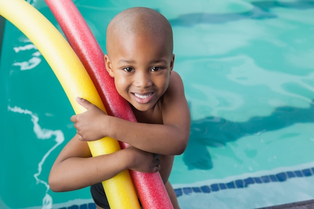 Menino pequeno segurando espuma de rolos junto à piscina