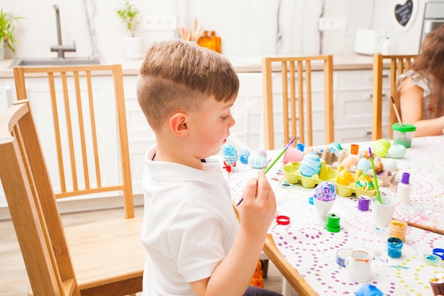 Menino pintando ovos em casa. Família feliz se preparando para a Páscoa.