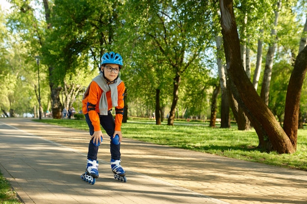 Menino pré-adolescente usando equipamento de proteção e patinação de capacete passando tempo ativo no parque urbano