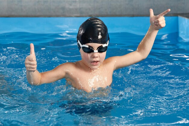 Menino pré-escolar aprendendo a nadar em uma piscina usando chapéu de natação e óculos de proteção