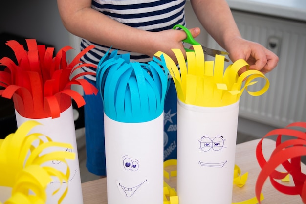 Menino pré-escolar cortando cabelo de papel com uma tesoura em cabeças engraçadas feitas à mão