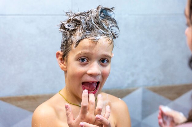 Foto menino pré-escolar lava a cabeça no banheiro com shampoo