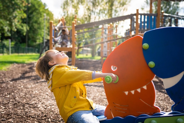 Foto menino pré-escolar no parque infantil feliz criança emocional balançando na prancha em um parque conceito de infância