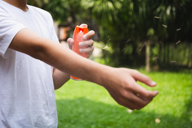 Foto menino pulverizando repelentes de insetos na pele no jardim com mosquitos voando