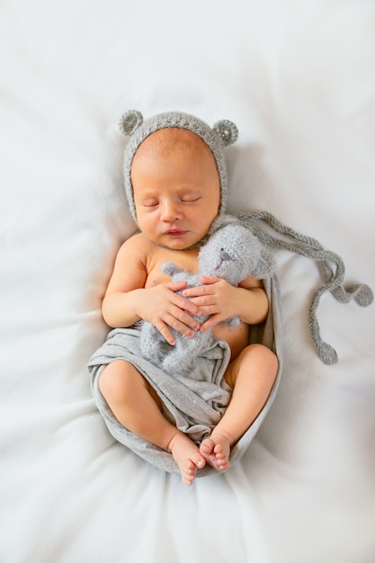 Menino recém-nascido dormindo em um terno cinza com orelhas e um brinquedo nas mãos.