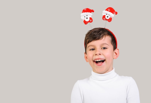 Foto menino rindo de 6 anos com chifres de brinquedo em forma de ursos de natal em fundo cinza isolado n