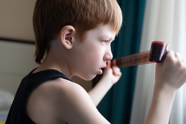 Menino ruivo infantil olha para a janela um filme para o retrato de close-up de estilo de vida de câmeras retrô antigas