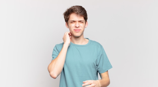 Menino se sentindo estressado, frustrado e cansado, esfregando o pescoço dolorido, com um olhar preocupado e preocupado