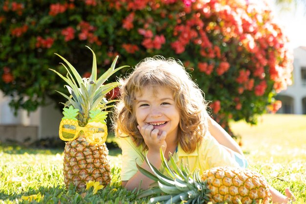 Menino segurando um abacaxi posando fundo de natureza de verão com espaço de cópia Frutos saudáveis para o conceito de crianças