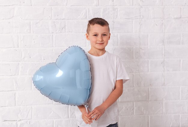 Menino segurando um balão em forma de coração azul na superfície branca